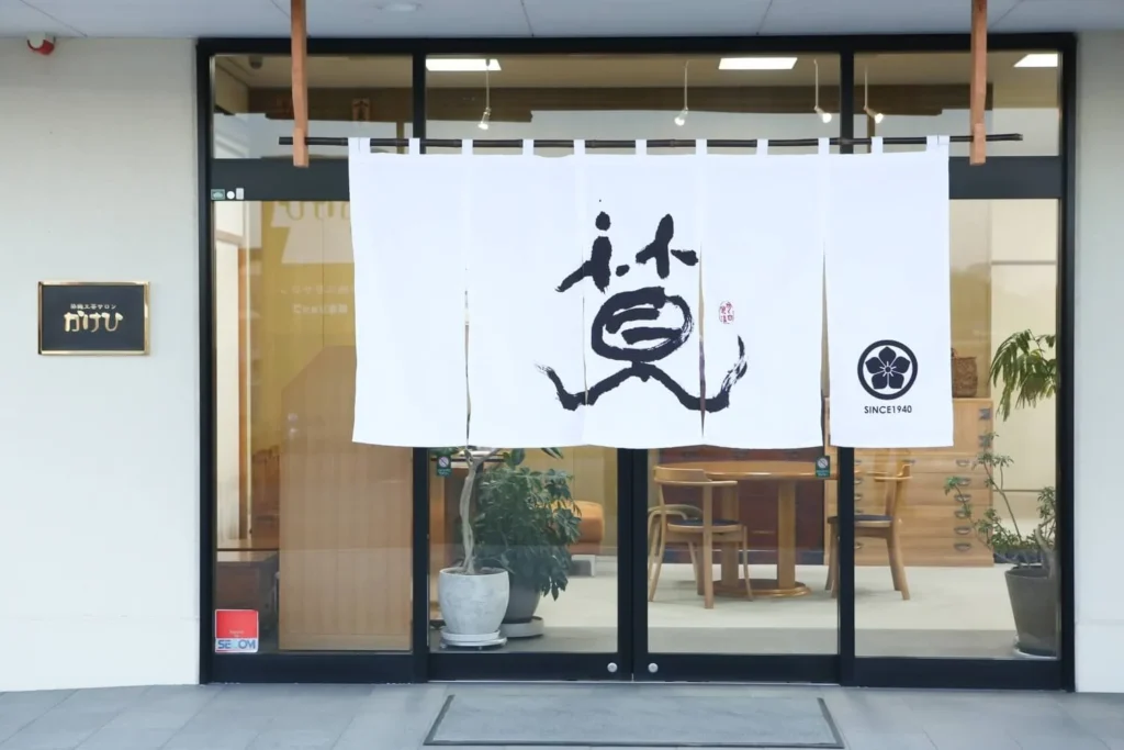 ANNACANEの和風モダンな店舗入口を、力強い筆文字とSINCE 1940の文字、家紋が描かれた白い暖簾が彩ります。