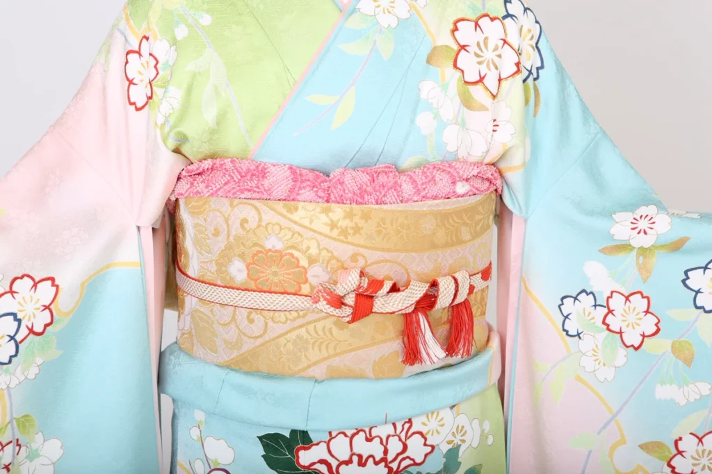 淡い水色と緑に桜柄が美しい着物に、金色の帯と紅白の帯締めを合わせた華やかな和装。